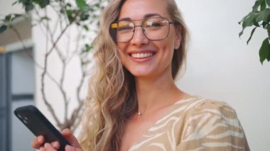 Gündelik giysiler içinde çekici genç bir kadın şehir caddesinde durmuş cep telefonuna bakıyor. Gülümseyen kız interneti tarıyor, arıyor, sosyal medyada haberleri okuyor..