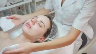 Kozmetik uzmanı, kadınların yüzlerini ve boyunlarını antibakteriyel peçetelerle siliyor. Doktor kozmetoloji kliniğinde güzellik prosedürü uyguluyor. Güzellik uzmanı güzellik kliniğinde hastaları temizliyor..