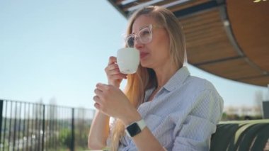 İş kadını restoran terasında sabah kahvesinin tadını çıkarıyor. Terasta kahve içen gözlüklü güzel bir kadın portreyi yakından çekiyor. Düşük açı görünümü