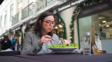 İş yemeği. İş kadını öğle arasında salata yiyor. Kafkasyalı, gözlüklü, açık kafede sağlıklı yemekler yiyen bir iş kadını. Salata yiyen ve konuşan bir kadın kafeteryada oturuyor.