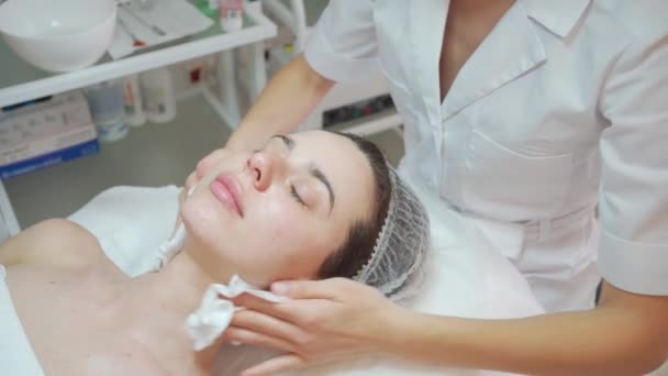 美容师在美容院用棉垫擦拭妇女的脸部和颈部 特写肖像 美容师在美容术中的皮肤清洁程序 美容业概念 医生们手挽手 — 图库视频影像
