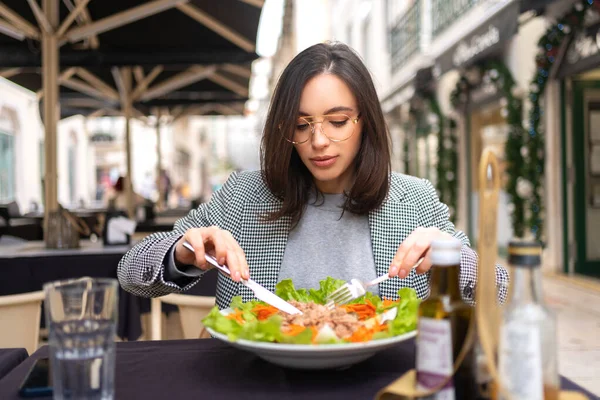 stock image Portrait attractive woman in glasses eating salad at cafe table. Beautiful young female enjoying fresh salad at nice restaurant.