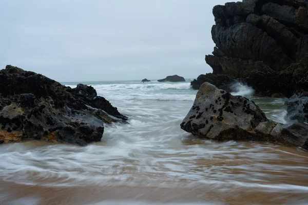 長い露出波が海岸の動きをクラッシュ白い波が夕暮れ時に岩をクラッシュ — ストック写真
