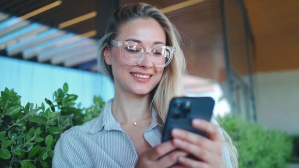 Happy Millennial Caucasian Girl Checking Social Media Holding Smartphone Smiling — стоковое видео