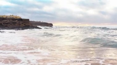Gün batımında okyanusun üzerinden uç. Bulutlu bir yaz gününde, Portekiz Praia da Guincho 'daki Atlantik Okyanusu sahilinde bir otel Praia da Guincho hava manzaralı. Dramatik gökyüzü, dağ plajı ve okyanus. Sinematik görünüm