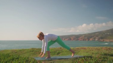 Son sınıf öğrencisi, yoga yapıyor, okyanus kıyısında asanas gösterisi yapıyor. Aktif emekli kadın vücuduna bakıyor ve güneşli bir sabahta hayatın tadını çıkarıyor. Emeklilik, rahatlama, tatil, sağlıklı yaşlı yaşam tarzı