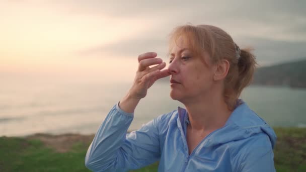 stock video Yogi female doing breathing exercises sitting on ocean shore. Senior woman performing breathing pranayama outdoors ocean background during sunset. Feeling harmony. Healthy senior lifestyle