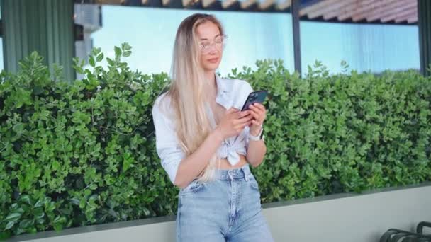 女性は屋外でスマートフォンを使用します ヨーロッパの街路の夏の日に立っているデバイススクリーンスマートフォンを見ている白人女性 エレガントな女性以外の技術を使用して携帯電話を使用する — ストック動画