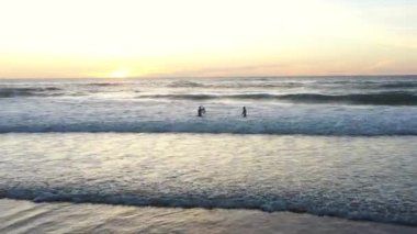 İki sörfçü gün batımında Atlantik Okyanusu 'nda dalgıç kıyafeti giyerek dalgalara binmek için antrenman yapıyorlar. Hava görünümü