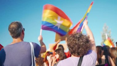 Gurur Yürüyüşü 'nü izleyen ve gökkuşağı bayrakları sallayan insanlar. LGBTQ bayrakları ve pankartlarıyla kalabalık. Cinsel eşitlik ve insan haklarına destek