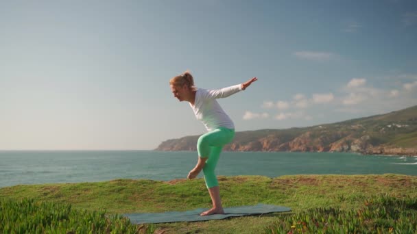 做瑜伽的老年妇女在海滨摆姿势 退休女性用一条腿做瑜伽气垫平衡身体 长大成人的女人在暑假里喜欢户外运动训练 健康的生活方式 — 图库视频影像