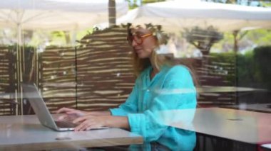 Dizüstü bilgisayar kullanan serbest çalışan bir kadın kahve dükkanında oturuyor ya da pencerenin arkasında ortak çalışıyor. Not defterinde çalışan mutlu, genç bir bayan. Pencere camından sokaktan bak