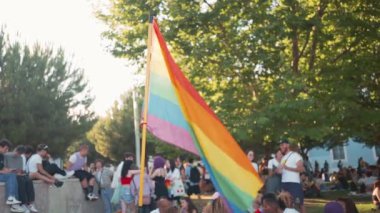 LGBT bayrağı rüzgârda dalgalanıyor. Gey gururlu insan kalabalığı arasında. Onur Yürüyüşü sırasında parkta dinlenen özgür insanlar 
