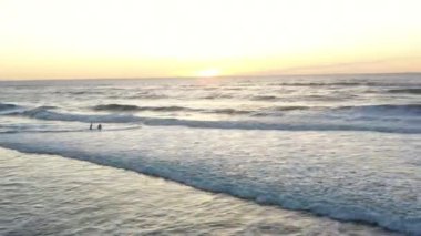 Sörfçü amatörler gün batımında okyanusta sörf tahtasına binerler. Hava görünümü