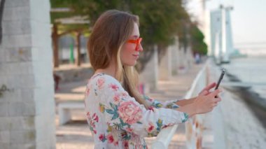 Moda gözlüklü Kafkas turist kadın gezinti alanında dururken cep telefonu kamerasıyla blog yazıları hazırlıyor. Kadın blog yazarı tatildeyken içerik yaratıyor