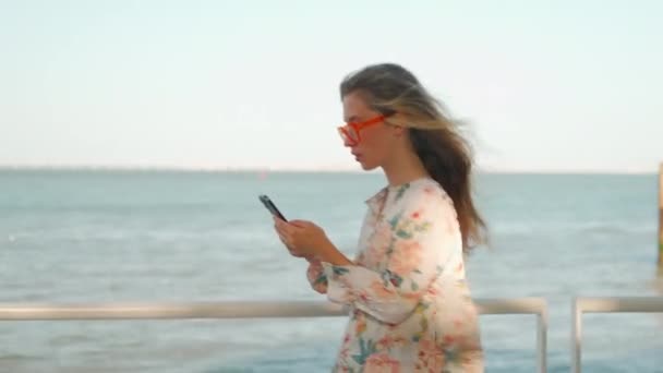 Elinde Akıllı Telefonuyla Yürüyen Çekici Genç Bir Kadın Var Çiçekli — Stok video