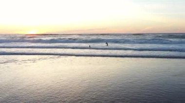 İki sörfçü arkadaş rengarenk yaz günbatımında büyük bir dalga oyuyorlar. Günbatımında okyanusta sörf yapan amatörler.