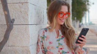 Gezinti güvertesinde cep telefonuyla sosyal medyayı kontrol eden çekici genç bir kadın. Beyaz kadın gözlük takıyor. Cihaz ekranlı. Akıllı telefon.