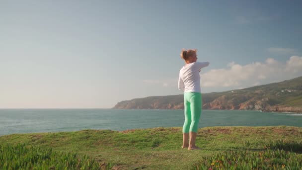 大姐在户外运动气功 新鲜空气上的体育活动 养恤金领取者妇女在海滨的草地上赤脚练气功 身体护理 体育活动概念 — 图库视频影像