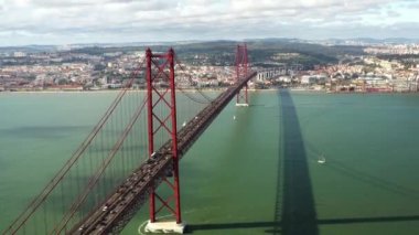 Portekiz, Lizbon 'da güneşli bir günde Tagus Nehri üzerindeki 25 de Abril Köprüsü panoramik dron görüntüsü kırmızı. Meşhur asma köprüden geçen yoğun araba trafiği. Ponte 25 de Abril Su üzerinde güzel gölgeler bırakıyor