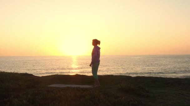 太陽の下でビーチでヨガをしている年金女性 海岸で健康のためにヨガアサナを練習する成熟した女性 ボディケア 身体活動のコンセプト エアリアルビュー — ストック動画