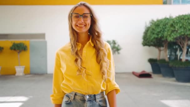 戴眼镜和黄色衬衫的女人笑着看着相机 阳光明媚的日子里 一个留着长长的波浪般的长发的金发女士在户外散步 — 图库视频影像