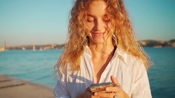 Sokakta Akıllı Telefonu Tutan Gülümseyen Bir Kadın Sarışın Kıvırcık Saçlı — Stok video