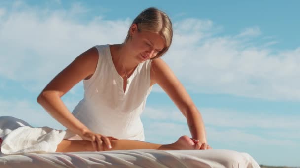在室外为女性手部按摩女性腿 专业的女按摩师给温泉按摩师客户躺在特殊的桌子上 蓝天作为背景 健康的生活方式和身体护理 — 图库视频影像