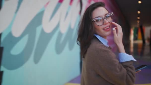 Kobieta Okularach Chodząca Jaskrawo Kolorowych Ścianach Uśmiechnięta Dama Trzymająca Telefon — Wideo stockowe