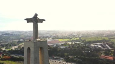 Portekiz 'deki Cristo Rei heykelinin etrafında dönüp duran insansız hava aracı. Panoramik kuşların gözü Almada, Tagus Nehri ve Lizbon 'da. Arka plandaki şehir manzarası ve mavi gökyüzünde İsa 'nın dev anıtı.