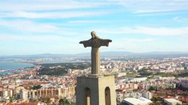 Portekiz. Güneşli yaz gününde Almada 'daki Cristo Rei heykelinin panoramik drone görüntüsü. Arka plandaki şehir manzarası ve mavi gökyüzünde İsa 'nın dev anıtı. 