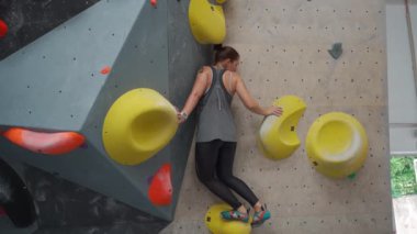 Kadın spor salonunda bir egzersiz dağına tırmanıyor. Yetişkin kadın tırmanma duvarında pratik yapıyor. Spor merkezinde kaya talimi yapan bir kadın, güvenlik ipi olmadan renkli yapay duvara tırmanan bir kadın.