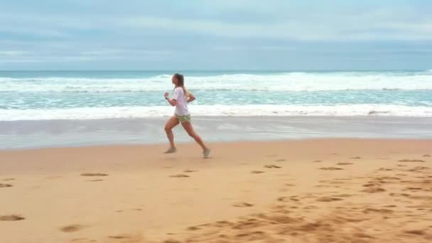 Spännande Flygdrönarbild Ung Kvinna Som Springer Längs Sandstranden Med Havsvågorna — Stockvideo