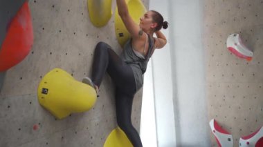 Spor salonundaki yapay duvara tırmanan gülümseyen sporcu kadının yan görüntüsü. Spor merkezinde kaya çalışması yapan azimli bir kadın. Sağlık ve zindelik kavramı. Yükseklik eğitimi
