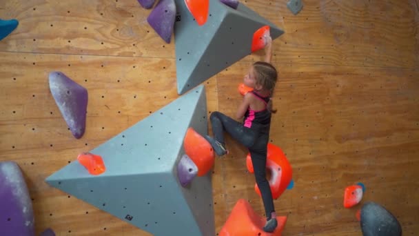 人工的な壁を登る少女 勇敢で強い女性の子供がモックウォールを登ります ボルダリングセンターのスポーティガールのフルボディ — ストック動画