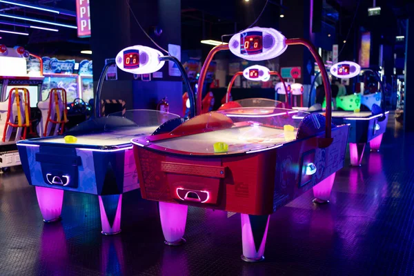 Air hockey tables illuminated neon light childrens entertainment center, accompanied by various gaming machines in an arcade.