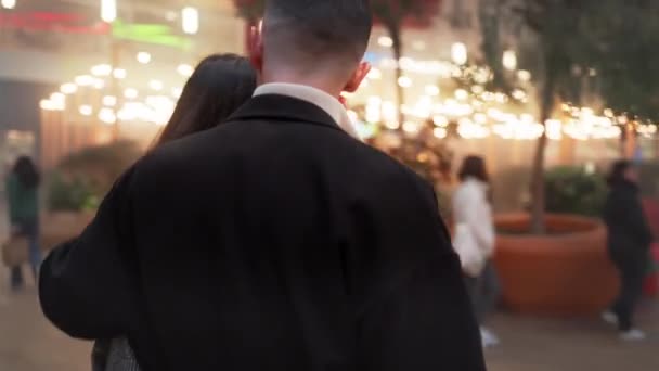 ロマンチックな若いカップルは 照らされた歩道を歩くトレンディな服 愛するパートナーは クリスマスの夜に街で話したりキスしたりします ショッピングバッグを持つ幸せな男と女性 — ストック動画