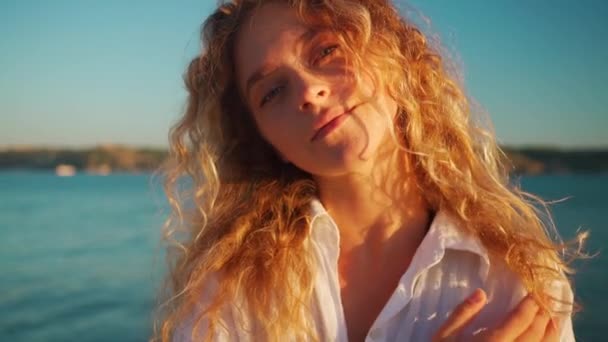 長い金髪の美しい若い女性の肖像画 カメラを見ている白いシャツの魅力的な女性 町の川の近くに立っている自信のある女性 — ストック動画