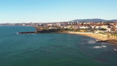Hava aracı görüntüsü turkuaz okyanus ve mavi gökyüzünün altında Atlantik okyanusu üzerinde dalgalar, şehir manzarası, Sao Pedro sahilleri ve güneşli bir günde Cascais, Portekiz 'de Estoril yapar.