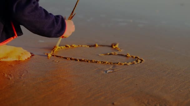Ugenkendelig Lille Pige Trækker Hjerte Form Fjer Sandstrand Ved Solnedgang – Stock-video