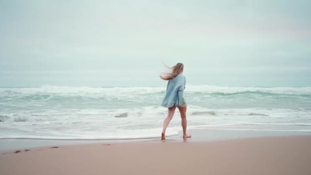 ハッピーな女性が海岸を走り回り カメラで微笑んでいる 幸せな女性の旅行者はデニムシャツウォークサンディービーチ 休暇を着た — ストック動画