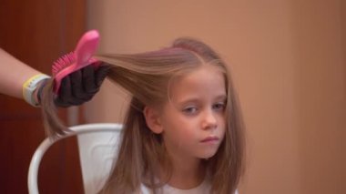 Anne evdeki kızına saç fırçası kullanarak pembe saç spreyi sürüyor. Hipoalerjenik saç spreyi kullanarak evde çocuk için kuaförlük.