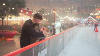 Buz pateni pistinin dışında şık giyinmiş mutlu çift. Noel gecesi öpüşen ve kucaklaşan romantik partnerler. Aydınlanmış şehirde kış tatili sezonu.