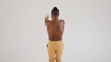 Beyaz arka planda gururla dans eden Afrikalı Amerikalı eşcinsel. Parlak makyajlı tişörtsüz genç erkek stüdyoda çeşitliliği ve kişisel karizmanın gücünü kutluyor..