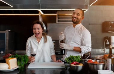 Yakışıklı genç Afrikalı şef, beyaz kız arkadaşıyla mutfakta kırmızı şarap malzemesi kullanarak yemek pişiriyor. Bir aşçı bir kıza nasıl yemek yapılacağını öğretir. Erkek ve kadın profesyonel mutfakta yemek pişiriyor..