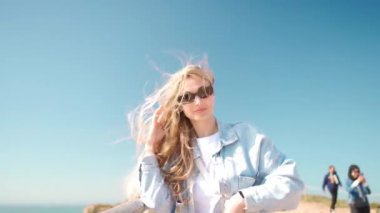 Genç kadın yüzüne yakın çekim rüzgarlı bir günde uçan saçlarla kaplı güneş gözlüğü takıyor. Rüzgarda uçuşan saçları olan bir kadın portresi. Gezgin arzusu sonbahar seyahati, atmosferik an. Yavaş çekim el bilgisayarı