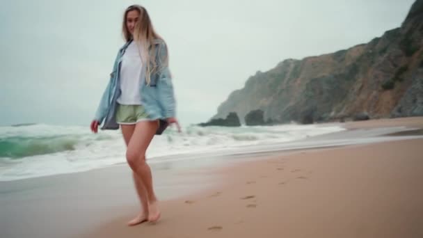 カメラで笑顔で海のビーチを走っている幸せな女性 幸せな女性の旅行者はデニムシャツウォークサンディービーチ 休暇を着た — ストック動画