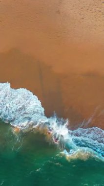 Hava aracı kumlu sahil şeridinde deniz dalgalarını vurdu. Dalgalar kıyı boyunca zarifçe koparken doğanın ritmi gelişiyor, dingin ve büyüleyici sahil manzarası yaratıyor. Dikey video