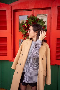 Avrupa şehrinde Noel tatili günü yürüyüş yapan Kafkasyalı mutlu kız. Esmer kadın şık bir ceket, ceket ve güneş gözlüğü takıyor. Olumlu duygular yaşam tarzı kavramı