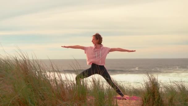 以秋季海洋观为背景的瑜伽练习 适合做瑜伽战士的女人在海滨摆姿势 健康的生活方式概念 中年女性练习瑜伽和关于自然的柔韧训练 — 图库视频影像